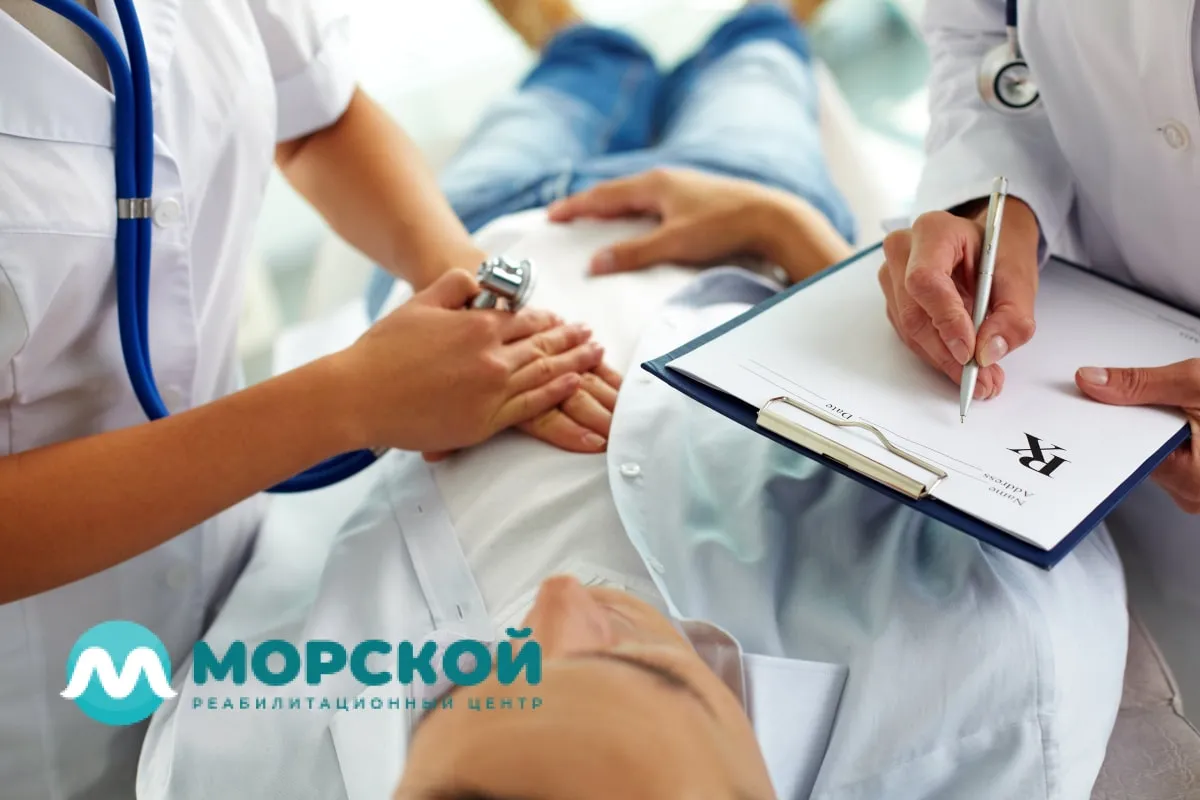 Два врача стоят перед пациенту около кушетки и проводят обследование больного