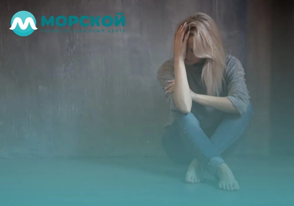 Женщина сидит в углу комнаты на полу и плохо себя чувствует